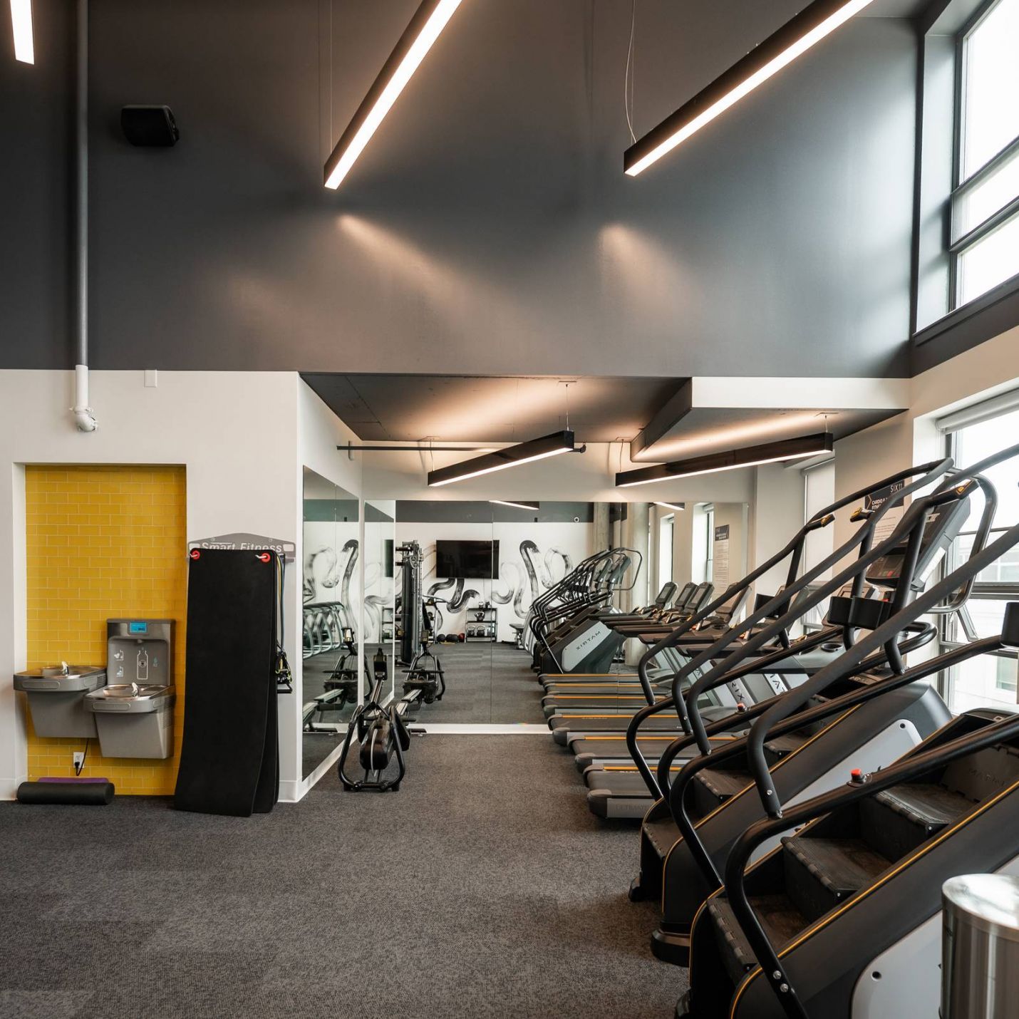 Six11 Student Living Apartments Modern gym with treadmills, stair machines, large mirrors, bright lighting, and a water fountain on the left.