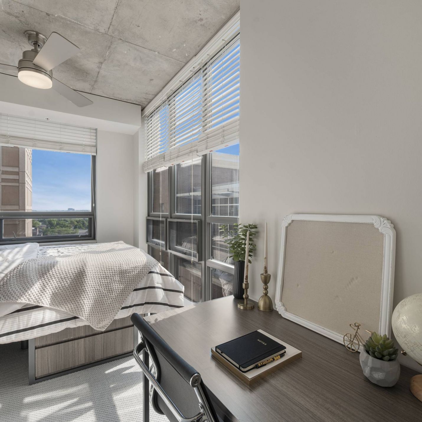 Six11 Student Living Apartments Bright bedroom with large windows, a bed, a desk with a globe, and modern decor, filled with natural light.