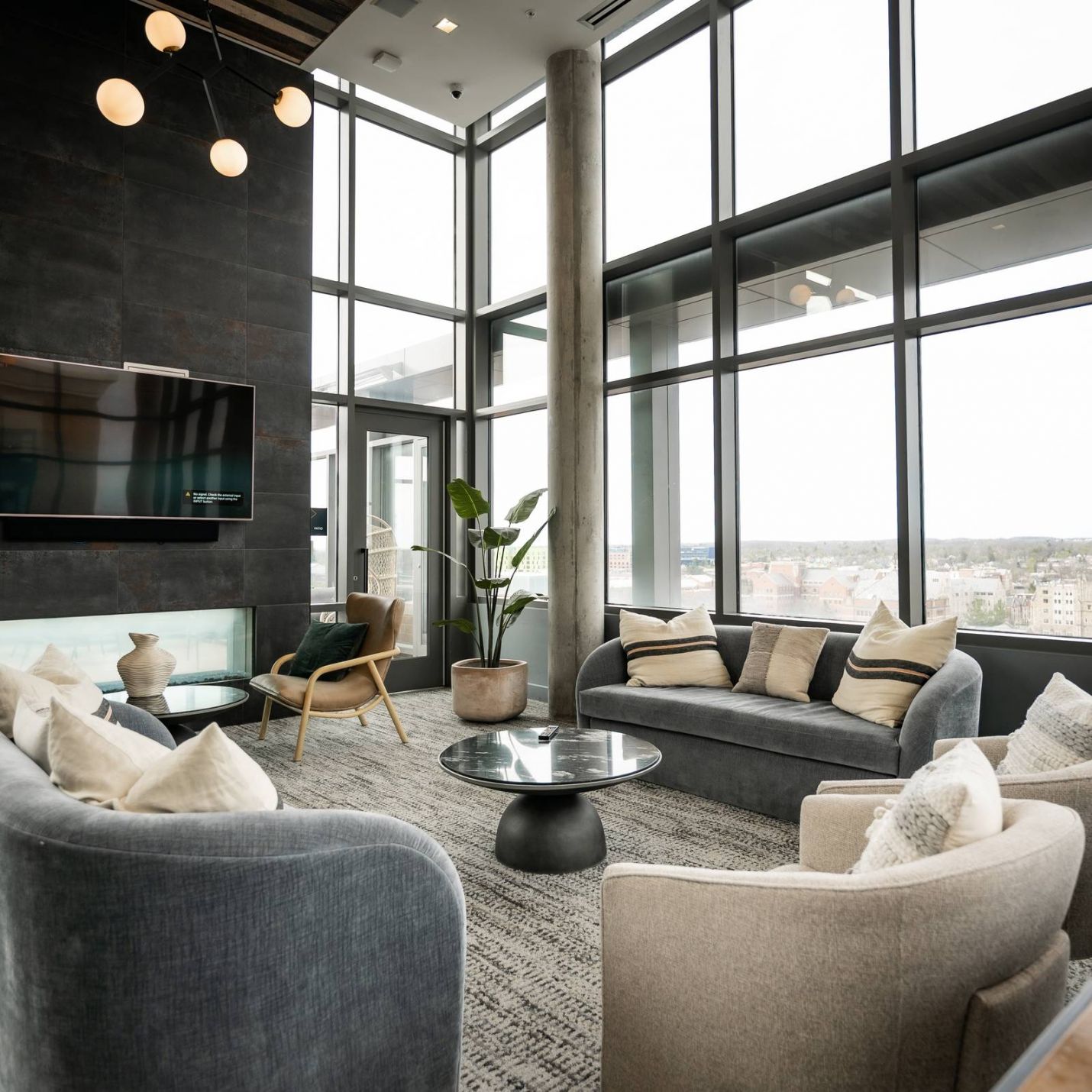 Six11 Student Living Apartments Modern lounge with large windows, gray sofas, armchairs, a coffee table, and city views outside.