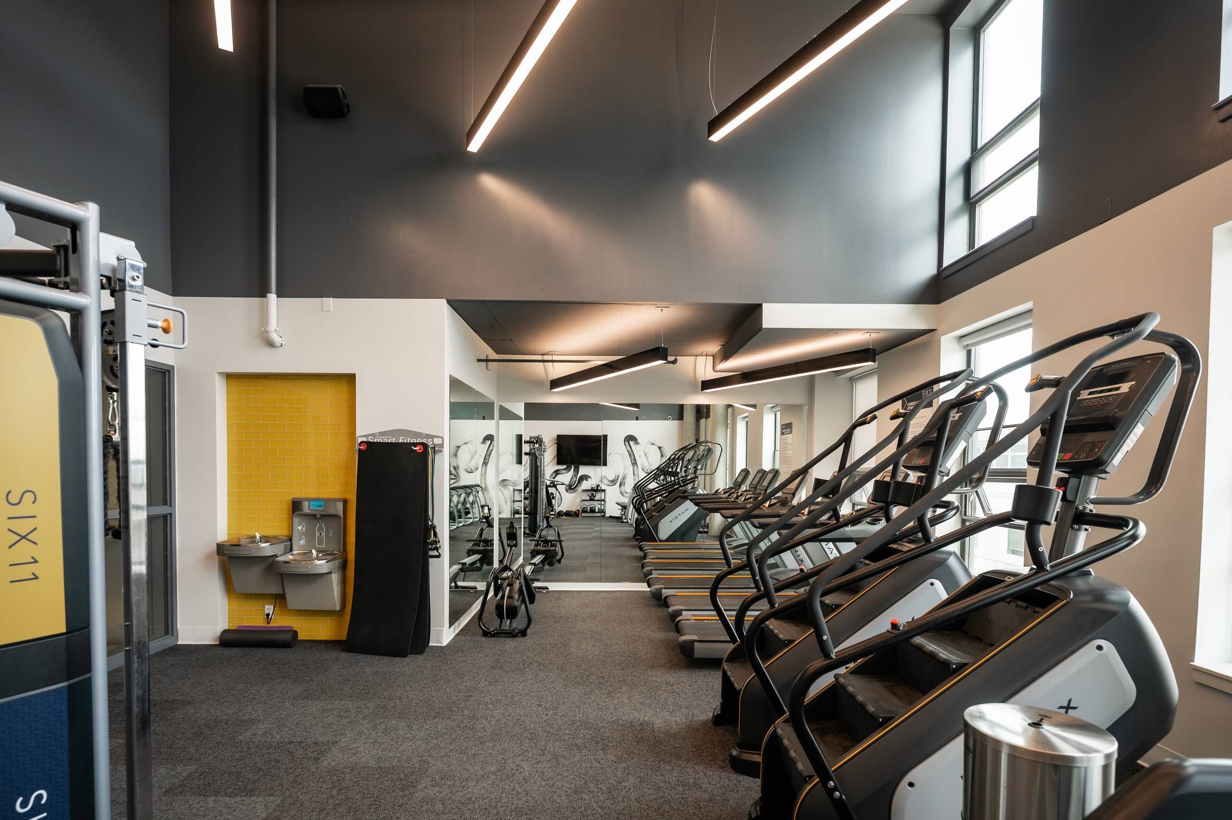 Six11 Student Living Apartments Modern gym with treadmills, stair machines, large mirrors, bright lighting, and a water fountain on the left.