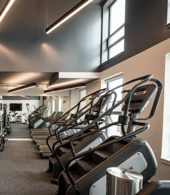 Six11 Student Living Apartments Modern gym with treadmills, stair machines, large mirrors, bright lighting, and a water fountain on the left.