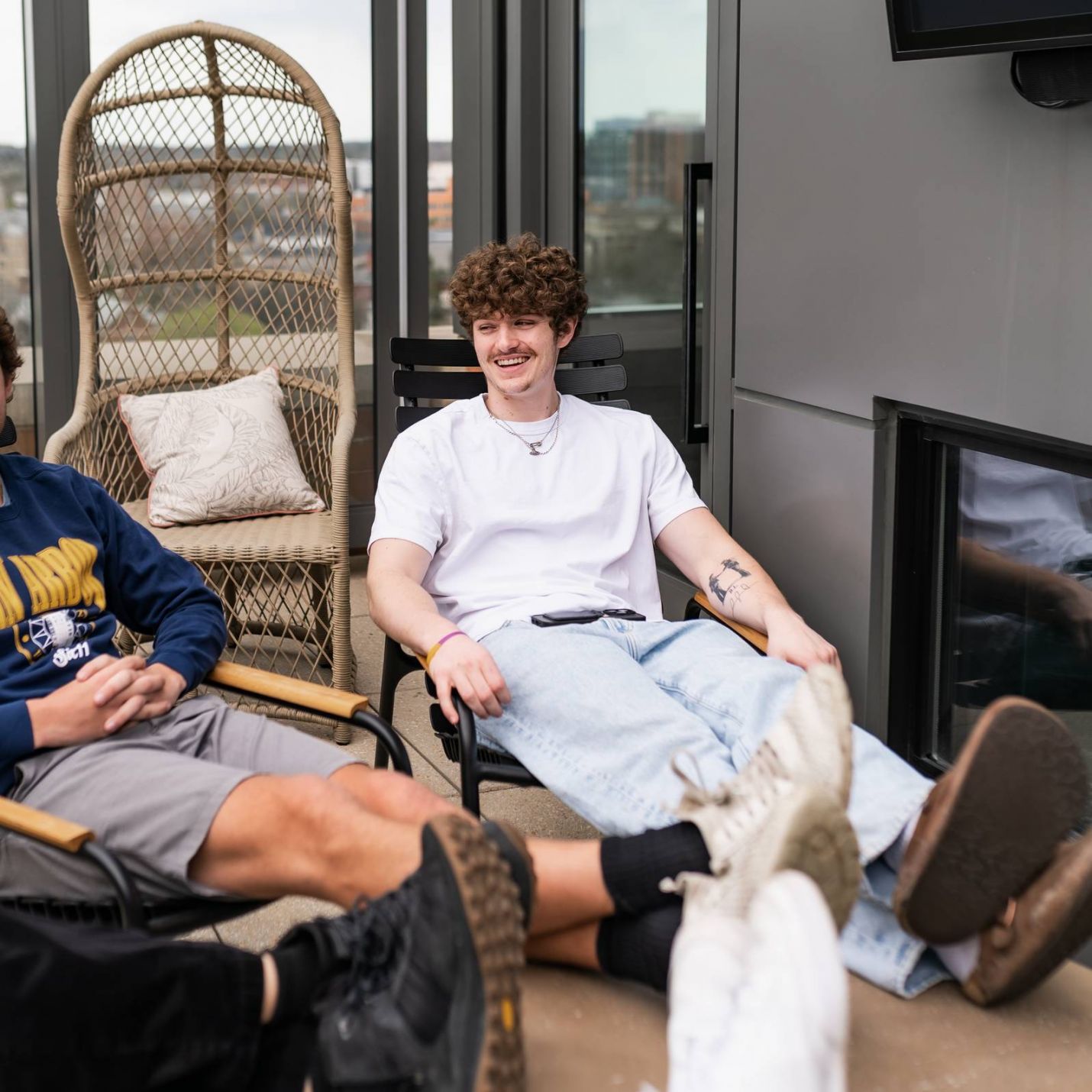 Six11 Student Living Apartments Three people relax outdoors, two with feet up on a table, while one smiles and sits back in a chair.