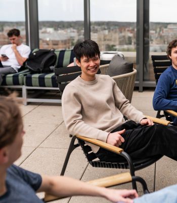 Six11 Student Living Apartments Three young men sit and chat on a rooftop patio, with one man smiling brightly in the center.