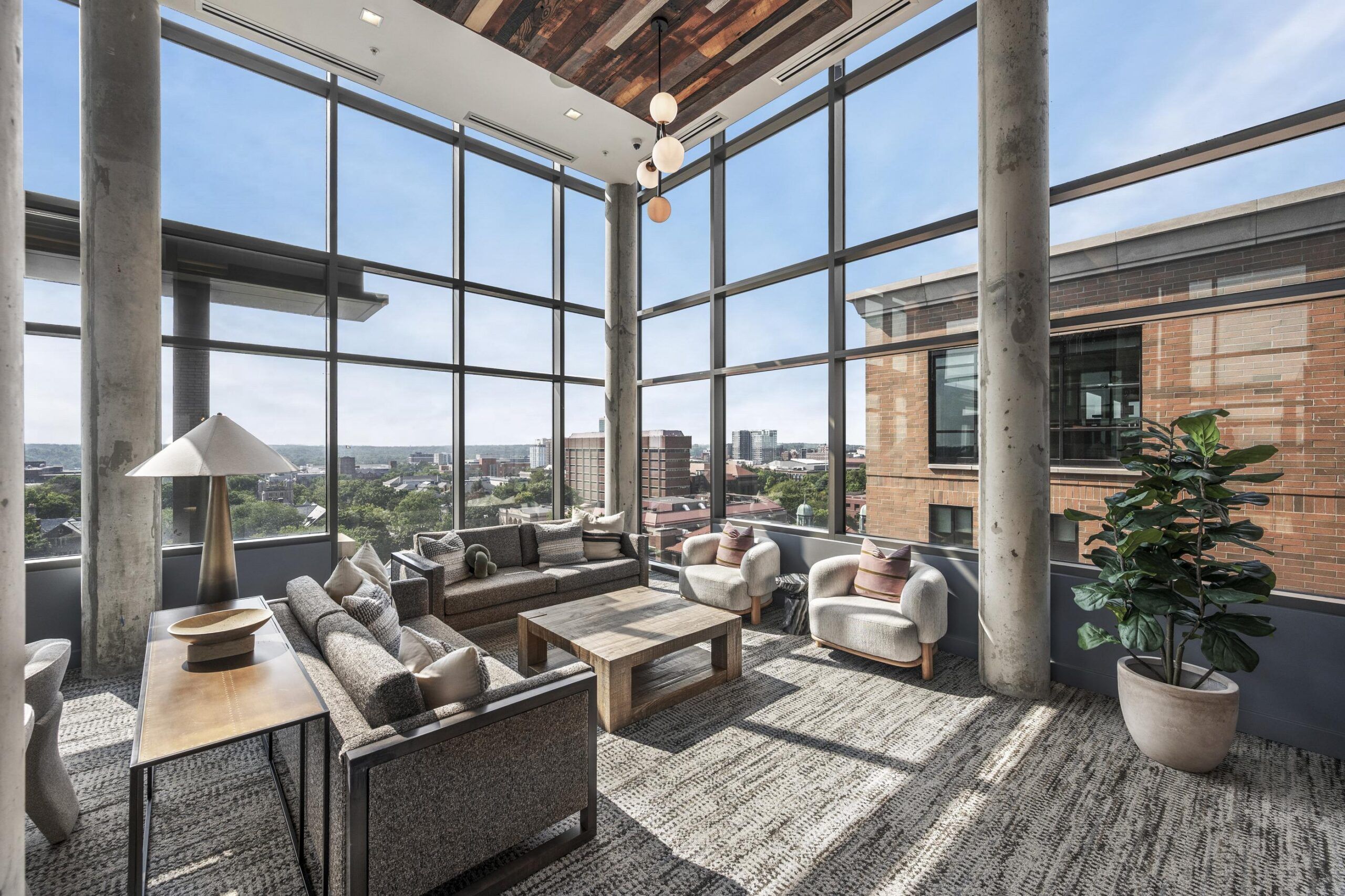 Six11 Student Living Apartments A modern lounge with floor-to-ceiling windows overlooking a city skyline, featuring gray sofas, two armchairs, and a wood coffee table.