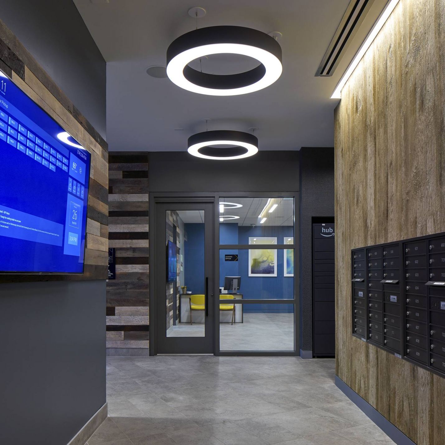 Six11 Student Living Apartments Modern hallway with circular ceiling lights, a wall TV screen, and rows of black mailboxes on the right.
