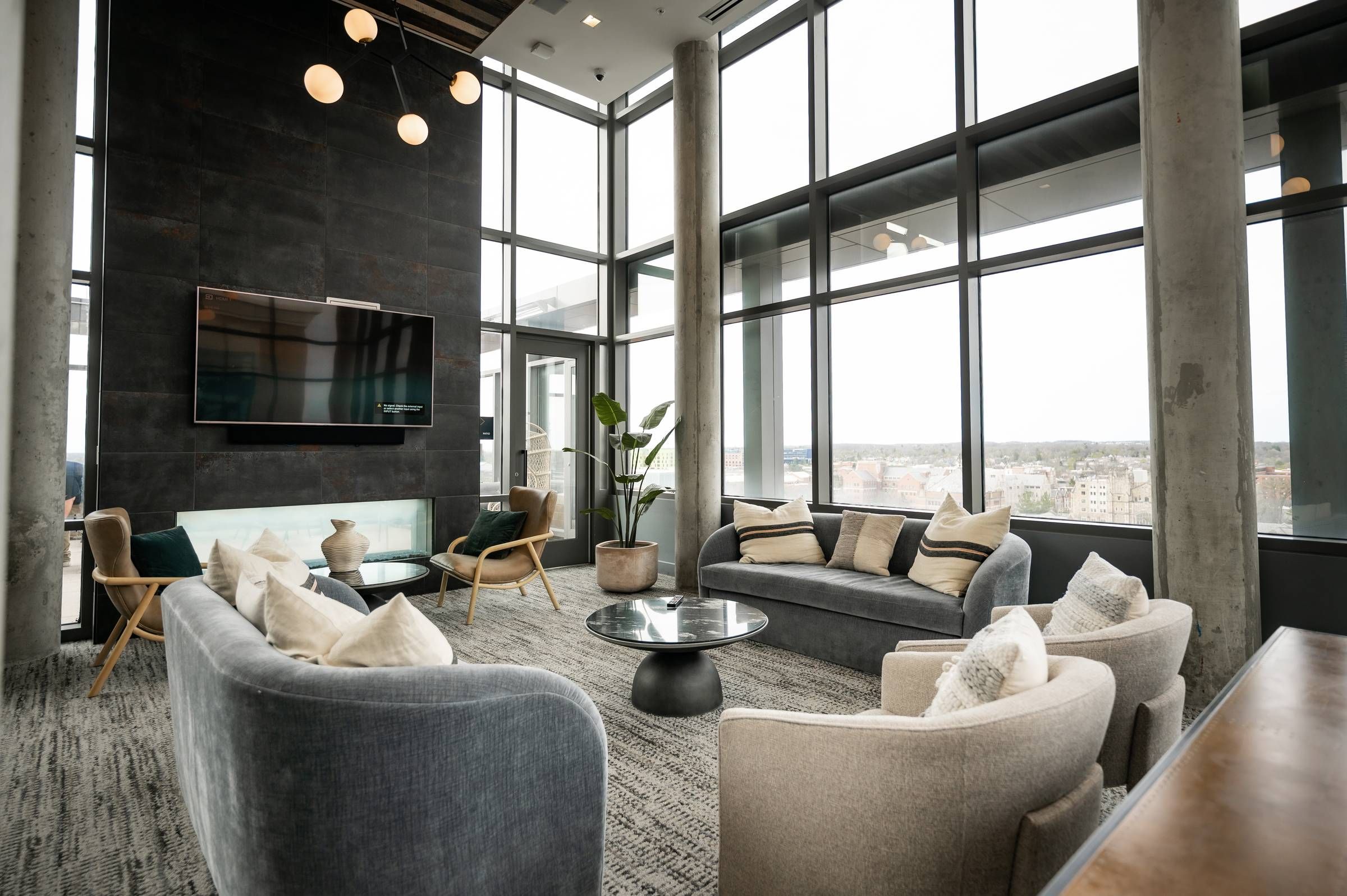 Six11 Student Living Apartments Modern lounge with large windows, gray sofas, armchairs, a coffee table, and city views outside.