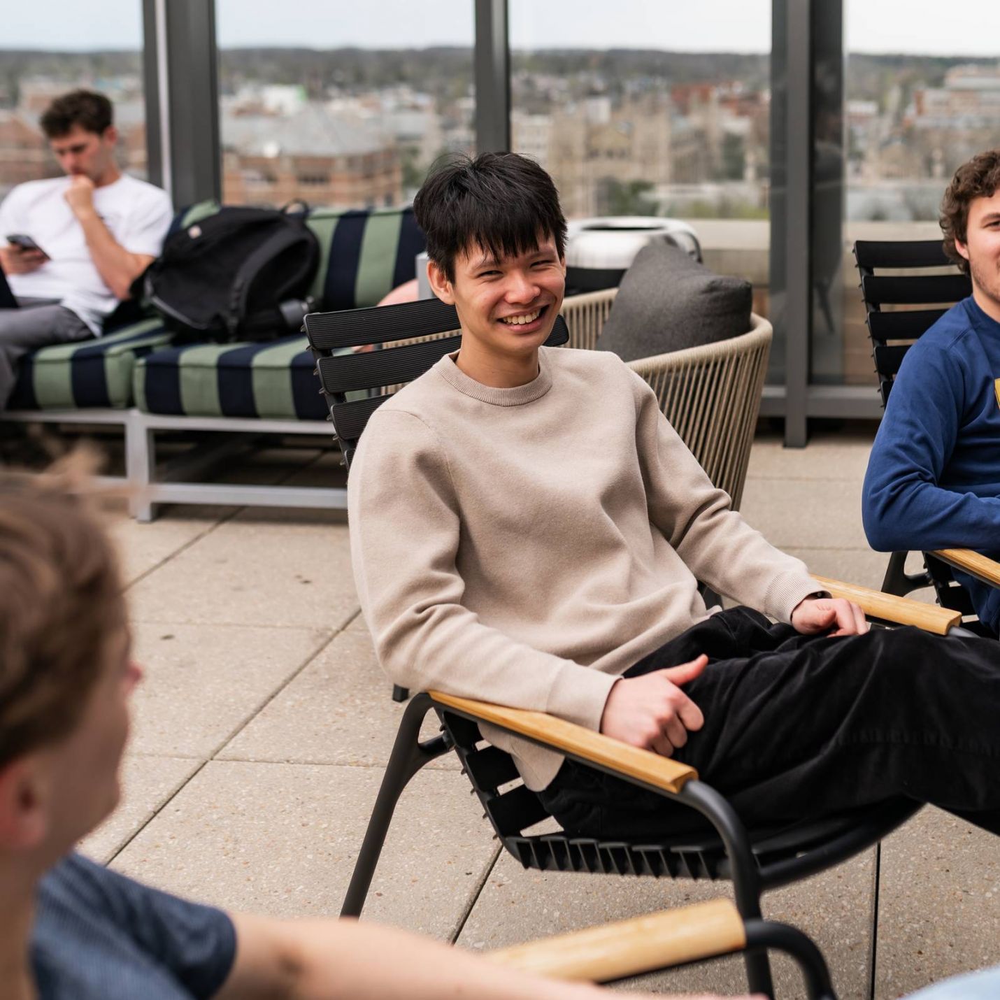Six11 Student Living Apartments Three young men sit and chat on a rooftop patio, with one man smiling brightly in the center.