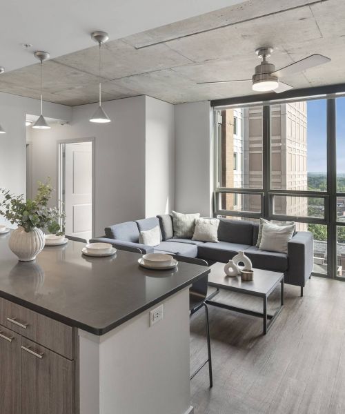 Six11 Student Living Apartments Modern apartment with a kitchen island, living area, large window, and city view.