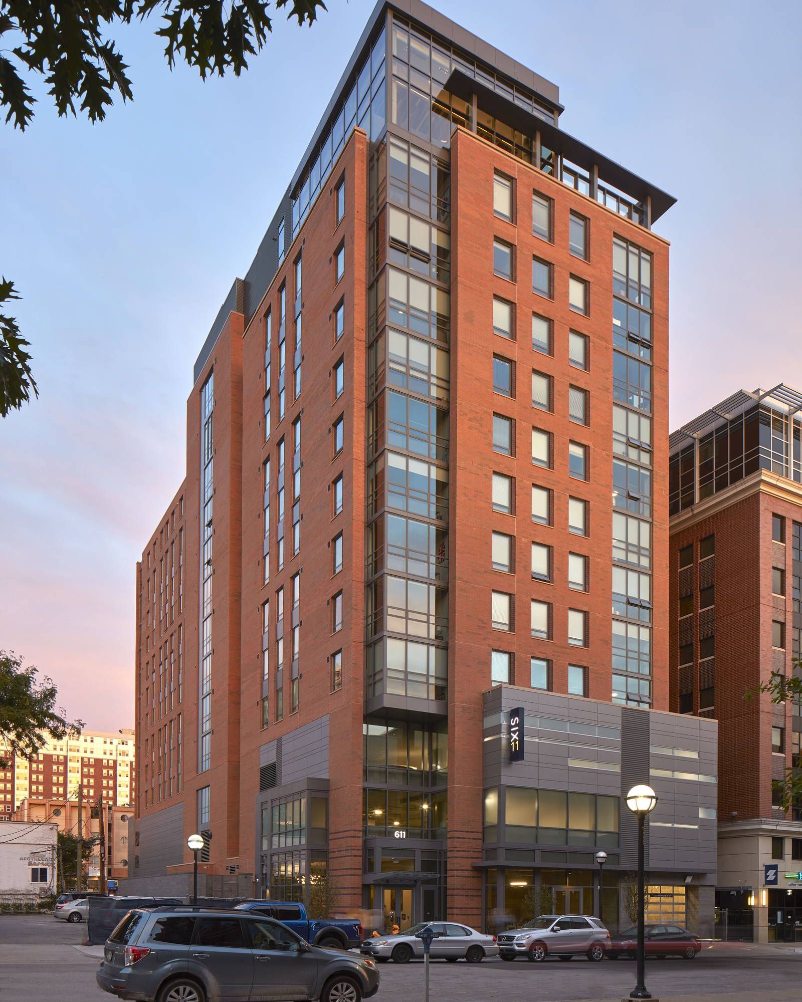 Six11 Student Living Apartments Tall modern brick building with large windows, cars parked in front, and trees partially visible on the sides.
