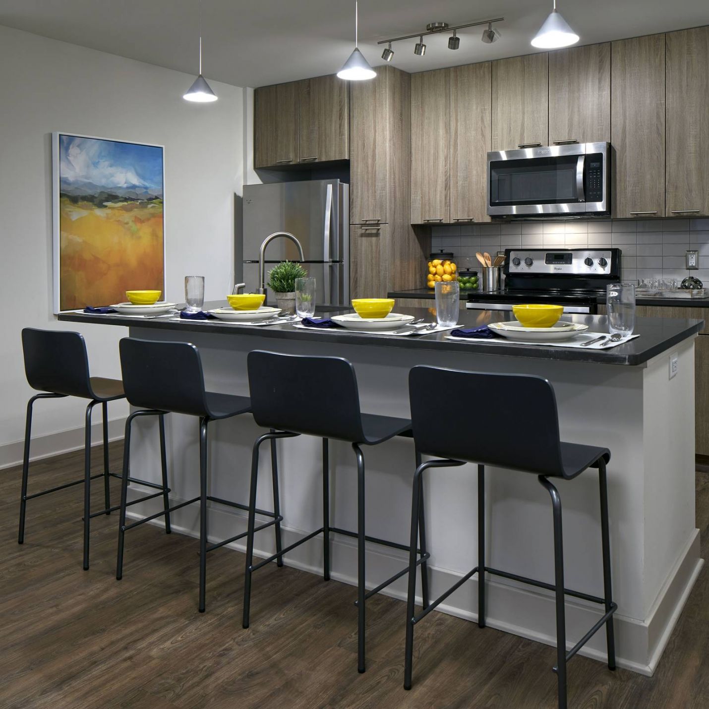 Six11 Student Living Apartments Modern kitchen with wood cabinets, stainless steel appliances, island seating, and colorful table settings.