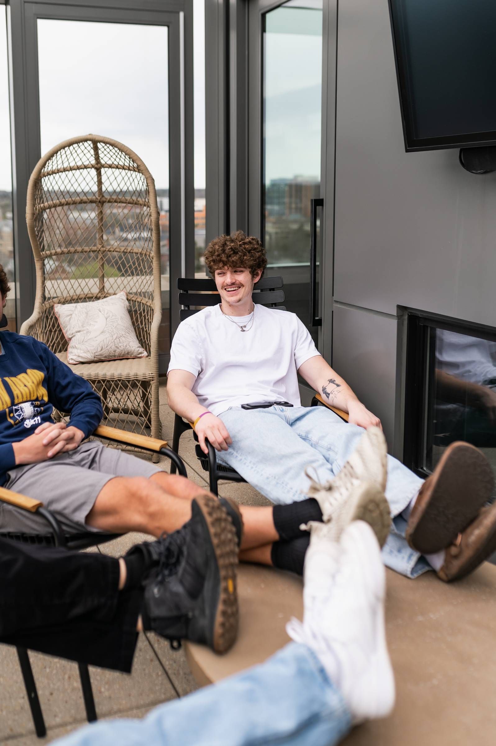 Six11 Student Living Apartments Three people relax outdoors, two with feet up on a table, while one smiles and sits back in a chair.