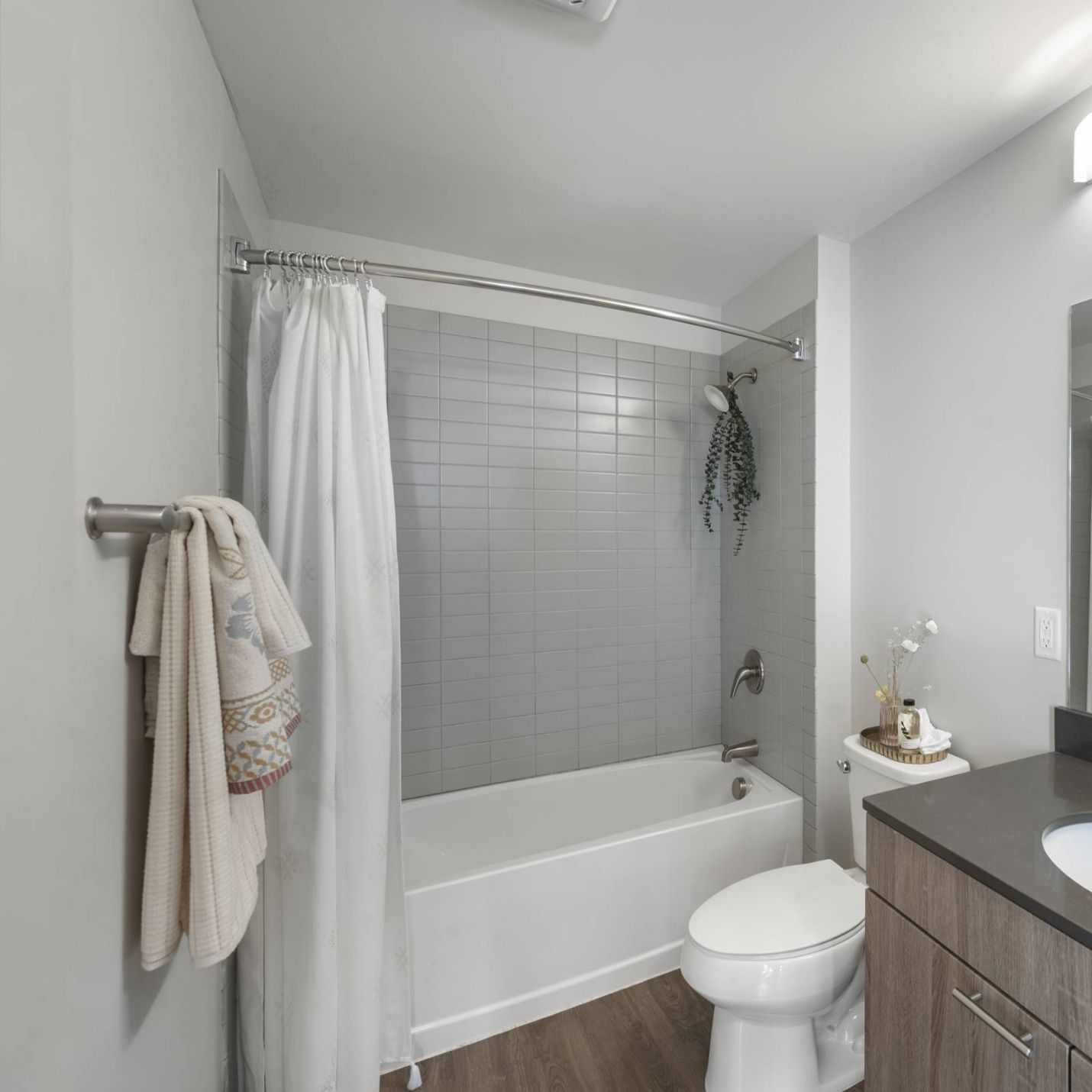 Six11 Student Living Apartments Modern bathroom with gray tiled tub, white shower curtain, dark vanity, and lighted mirror.